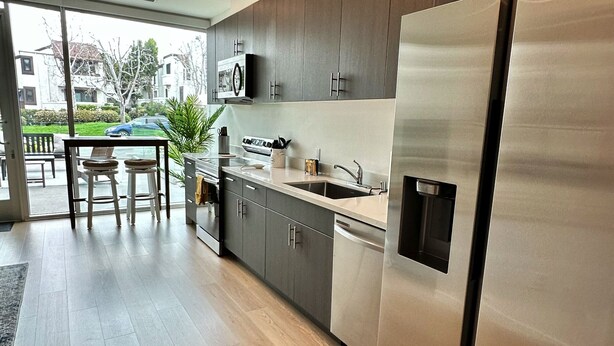 A modern kitchen with stainless steel appliances, wooden cabinets, and a dining area with a table and chairs. - Clean, bright, with large exclusive patio, parking, close to airport and beach (San Diego)