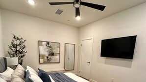 A bedroom with a bed, a ceiling fan, a wall-mounted TV, and a door. - Clean, bright, with large exclusive patio, parking, close to airport and beach (San Diego)