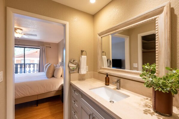 Habitación de hotel con cama, baño con lavamanos y espejo, y balcón con vistas.