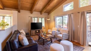 A cozy living room with a wooden ceiling, a large flat-screen TV, a dark leather sofa, plaid chairs, and a coffee table with snacks. - Luxury Tahoe Escape - Rec Room - Pickleball - Golf (Incline Village)