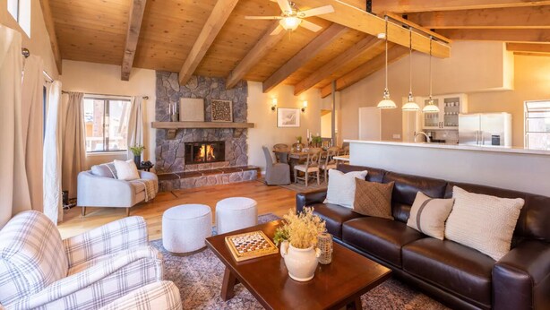 A spacious living room with a stone fireplace, wooden ceiling beams, and a dining area with a kitchen in the background. - Luxury Tahoe Escape - Rec Room - Pickleball - Golf (Incline Village)