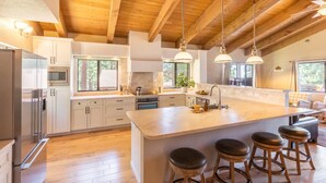 A modern kitchen with wooden beams, a large island with stools, and a dining area with a view of trees. - Luxury Tahoe Escape - Rec Room - Pickleball - Golf (Incline Village)