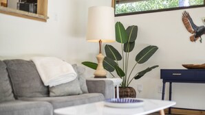 Ein Wohnzimmer mit grauem Sofa, einem weißen Couchtisch, einer Lampe, einer großen Pflanze, einer Wanddekoration mit einem Adler und einem dunkelblauen Beistelltisch.
