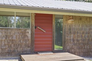 Une cabane en bois avec une porte rouge, le numéro « 103 » peint sur le mur et un petit porche.