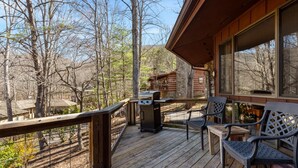 A wooden deck with outdoor seating, a grill, and a view of a cabin in the background. - Cornerstone Cabin at Springdale (Haywood County)