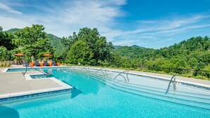 A swimming pool with clear blue water, surrounded by lush greenery and hills in the background. - Cornerstone Cabin at Springdale (Haywood County)