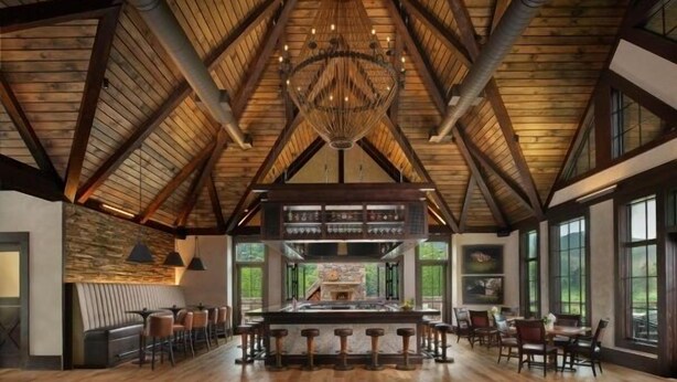 A spacious room with a high wooden ceiling, a central fireplace, and a bar area with stools. - Cornerstone Cabin at Springdale (Haywood County)
