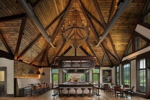 A spacious room with a high wooden ceiling, a central fireplace, and a bar area with stools.