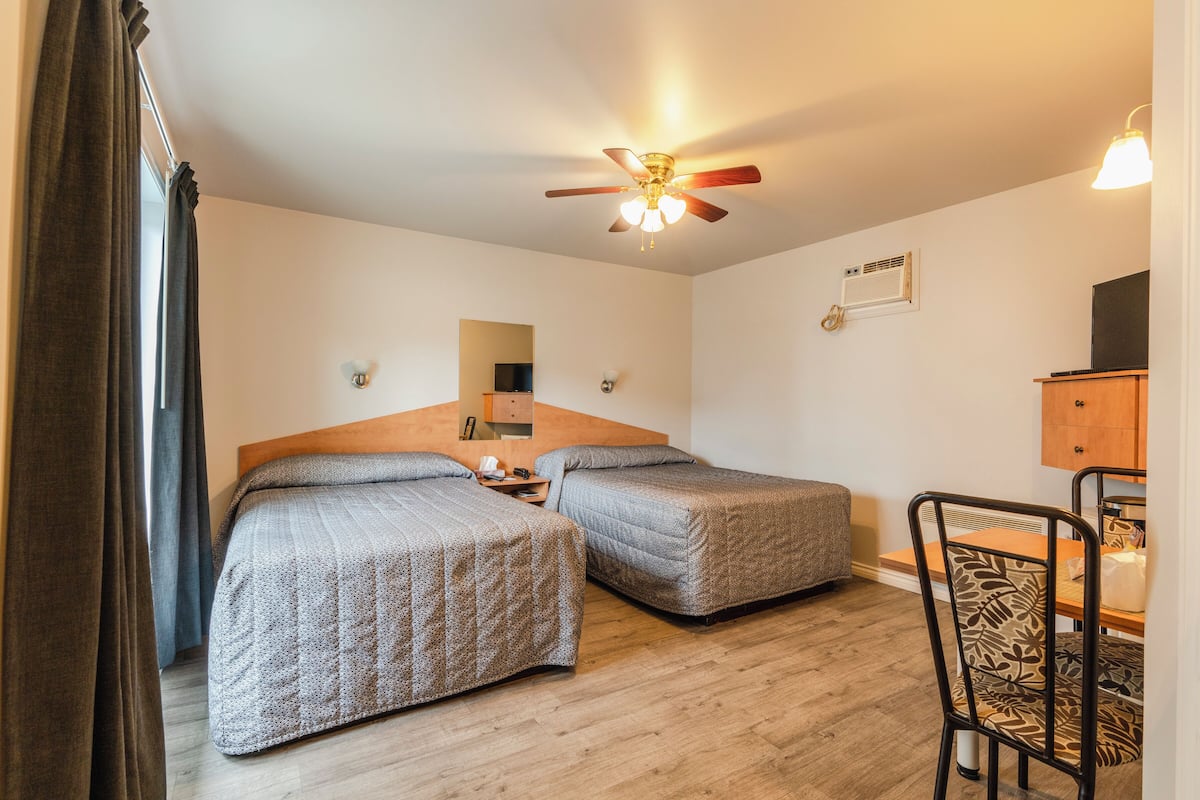 A room with two beds, a ceiling fan, a wooden table, and a chair.