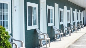 A row of motel rooms with white-framed windows and doors, numbered sequentially, and a row of plastic chairs outside. - Motel Park (Val-d'Or)