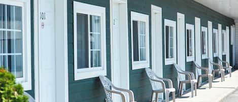 A row of motel rooms with white-framed windows and doors, numbered sequentially, and a row of plastic chairs outside.