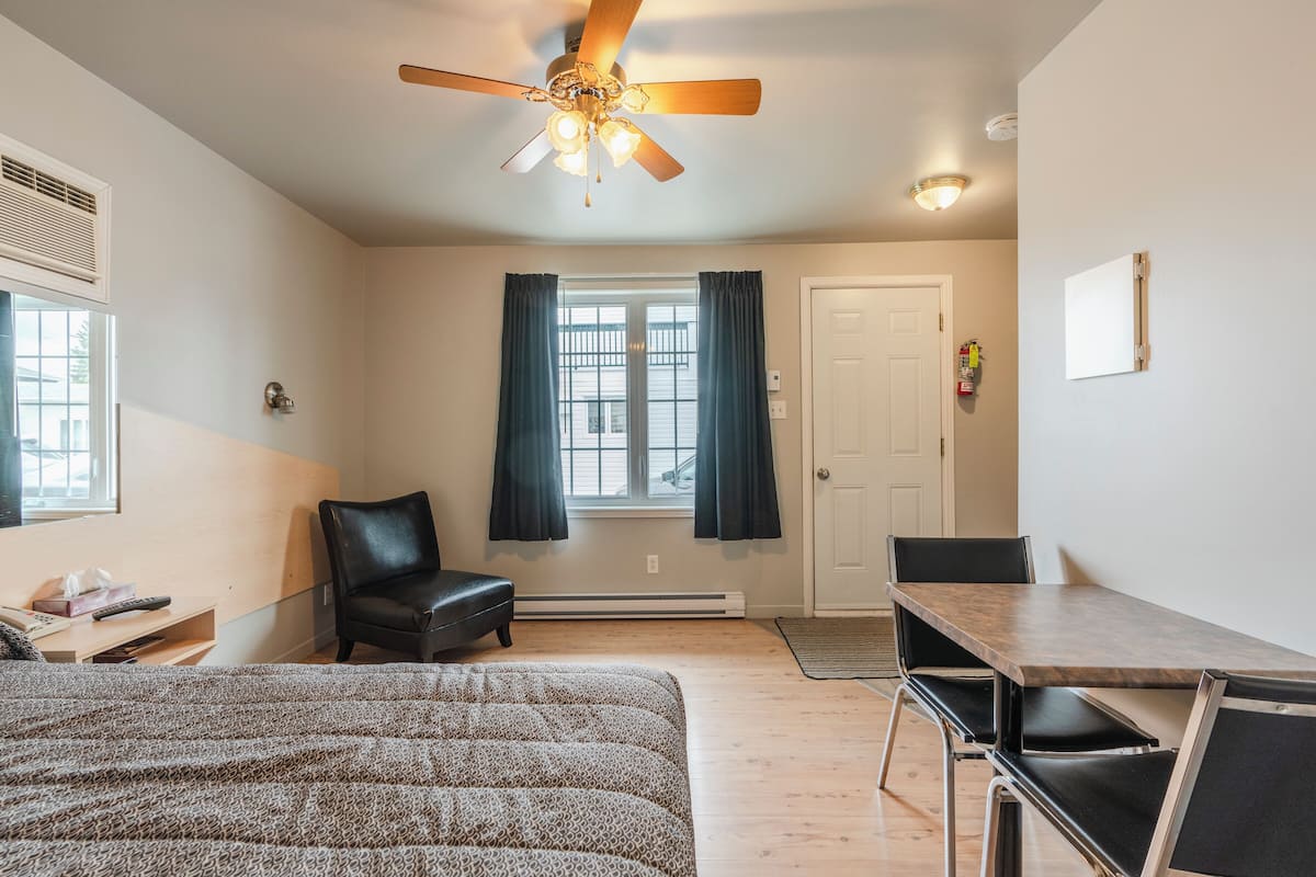 A bedroom with a bed, a desk, a chair, a ceiling fan, and a window with curtains.
