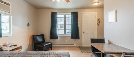 A bedroom with a bed, a desk, a chair, a ceiling fan, and a window with curtains.