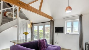 A modern living room with a purple sofa, a staircase, a TV mounted on the wall, and a large window. - 2 bedroom accommodation in Aldeby, near Beccles (Aldeby, near Beccles)