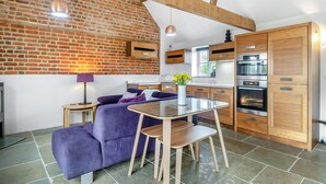 A modern kitchen with wooden cabinets, a built-in oven, and a dining area with a glass table and purple sofa. - 2 bedroom accommodation in Aldeby, near Beccles (Aldeby, near Beccles)