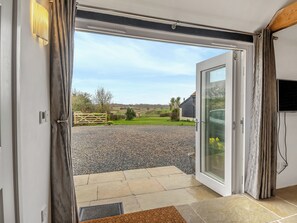 An open door leading to a gravel driveway, a wooden gate, and a view of a rural landscape.