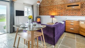 A modern kitchen with a brick wall, a glass table, purple furniture, and a fireplace. - 2 bedroom accommodation in Aldeby, near Beccles (Aldeby, near Beccles)