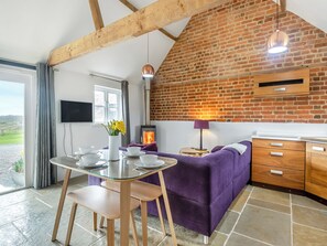 A modern kitchen with a brick wall, a glass table, purple furniture, and a fireplace. - 2 bedroom accommodation in Aldeby, near Beccles (Aldeby, near Beccles)