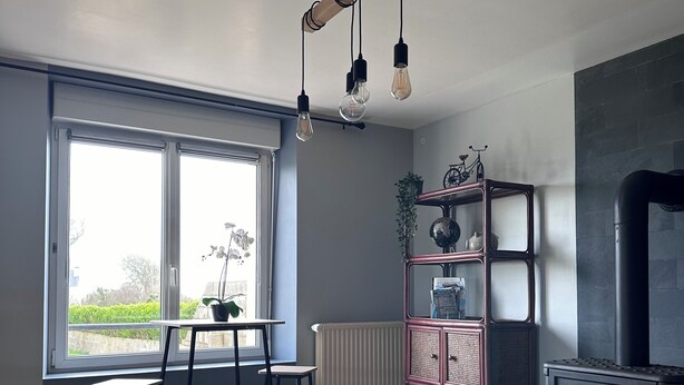A modern living room with a large window, a fireplace, a dining area with chairs, and a bookshelf.
