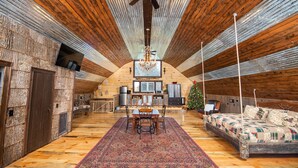 Ein gemütliches Dachzimmer mit Holzwänden und schrägen Decken, mit Esstisch, Stühlen, einem Weihnachtsbaum und einem Bett.
