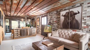 Ein rustikales Interieur mit freiliegenden Holzbalken, einer Ziegelwand, einer Couch und einem Essbereich mit Holztisch und Stühlen.
