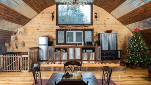 Ein gemütliches Blockhaus-Interieur mit Holzausstattung, einem Essbereich mit Tisch und Stühlen, einer Küche mit Kühlschrank und Schränken sowie einem Weihnachtsbaum.