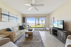 A living room with a beige sofa, a coffee table, a television on a wooden cabinet, and a view of the outdoors through large sliding glass doors.