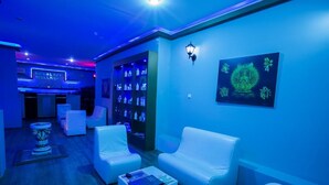 A room with white leather sofas, a small table, and a wall-mounted shelf with bottles. - Seven Seas Palmeras Bay (Alanya)