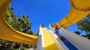 A water slide with a yellow and white design, surrounded by palm trees and clear blue sky. - Seven Seas Palmeras Bay (Alanya)