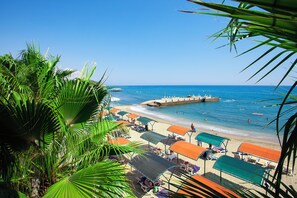 Ein Strand mit Sonnenschirmen, Liegestühlen, einem Steg und klarem, blauem Wasser.