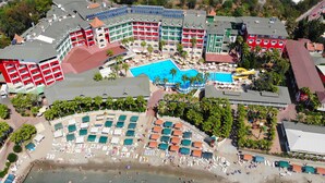 An aerial view of a resort with multiple buildings, a central swimming pool, and a beach area with sun loungers and umbrellas. - Seven Seas Palmeras Bay (Alanya)