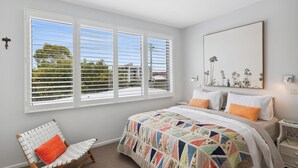 A bedroom with a large bed, a chair, and a window with blinds.