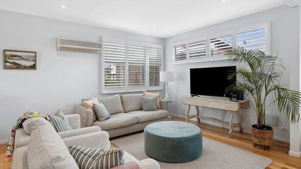 A modern living room with a sofa, ottoman, and a television on a stand.