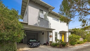 A modern two-story house with a garage, a black car parked inside, and a well-maintained garden.