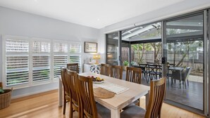 A dining area with a wooden table and chairs, a buffet table with fruits, and a view through large glass doors to an outdoor patio.