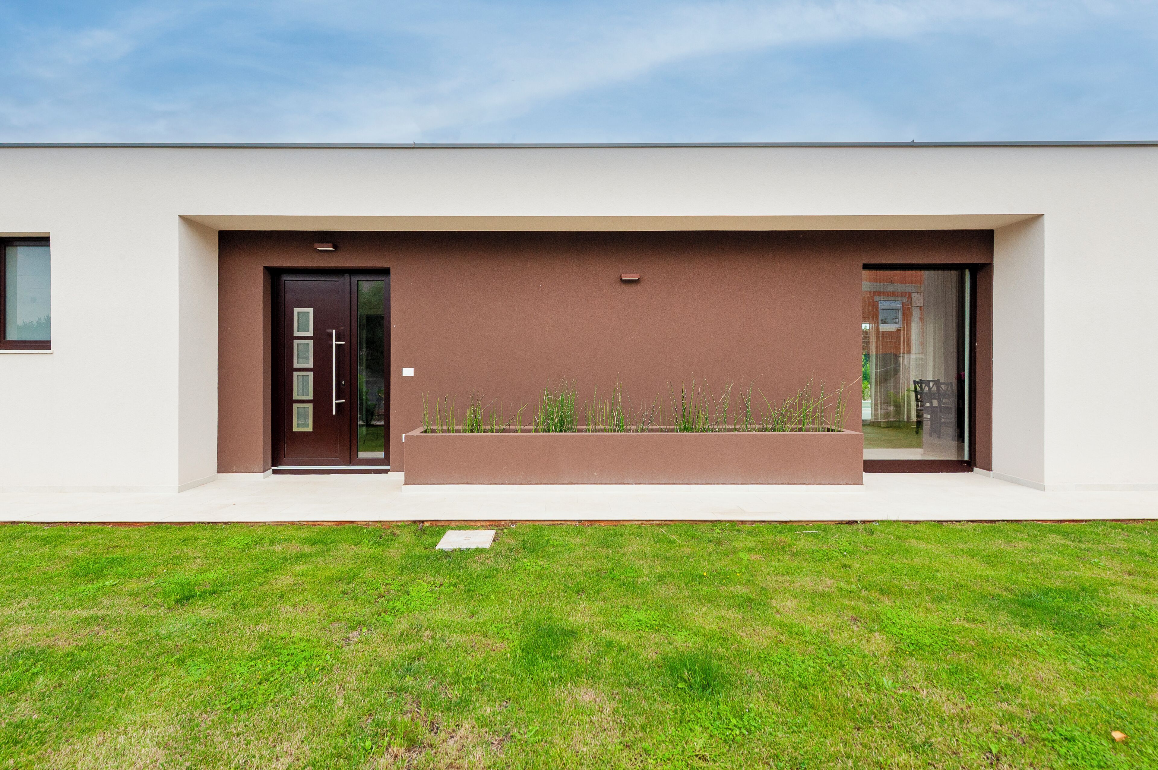 A modern building with a flat roof, a brown facade, and a large window.