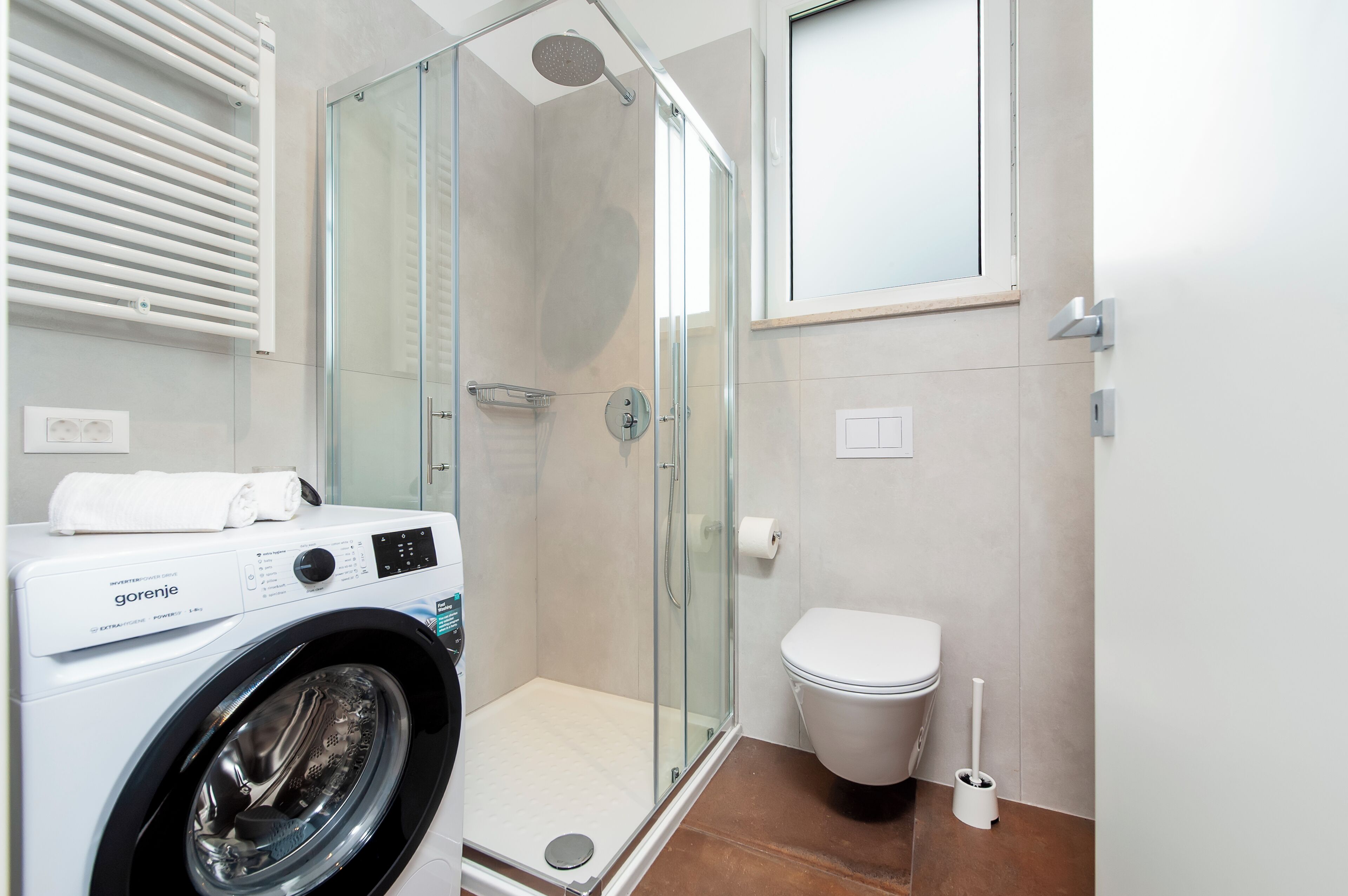 Een moderne badkamer met een glazen douchecabine, een wasmachine en een toilet.