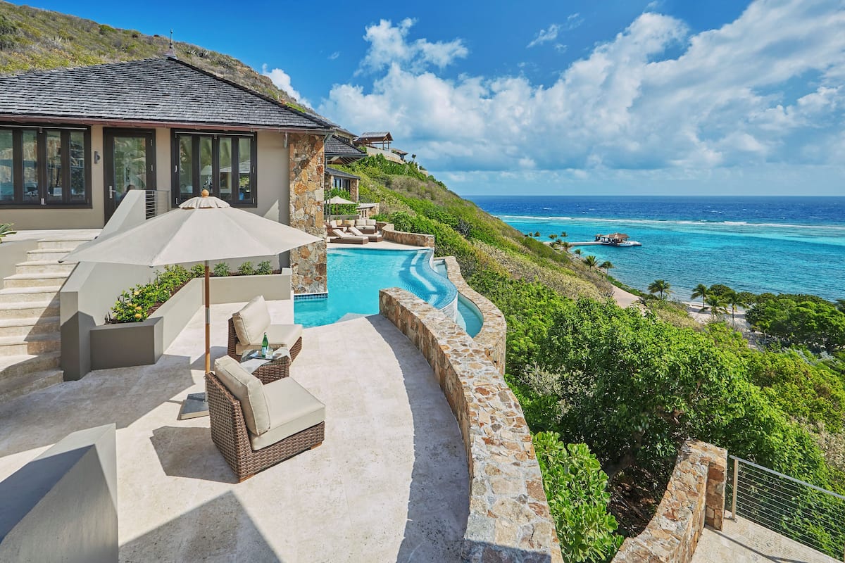A luxurious outdoor pool area with a stone wall, a lounge chair, and a large umbrella.