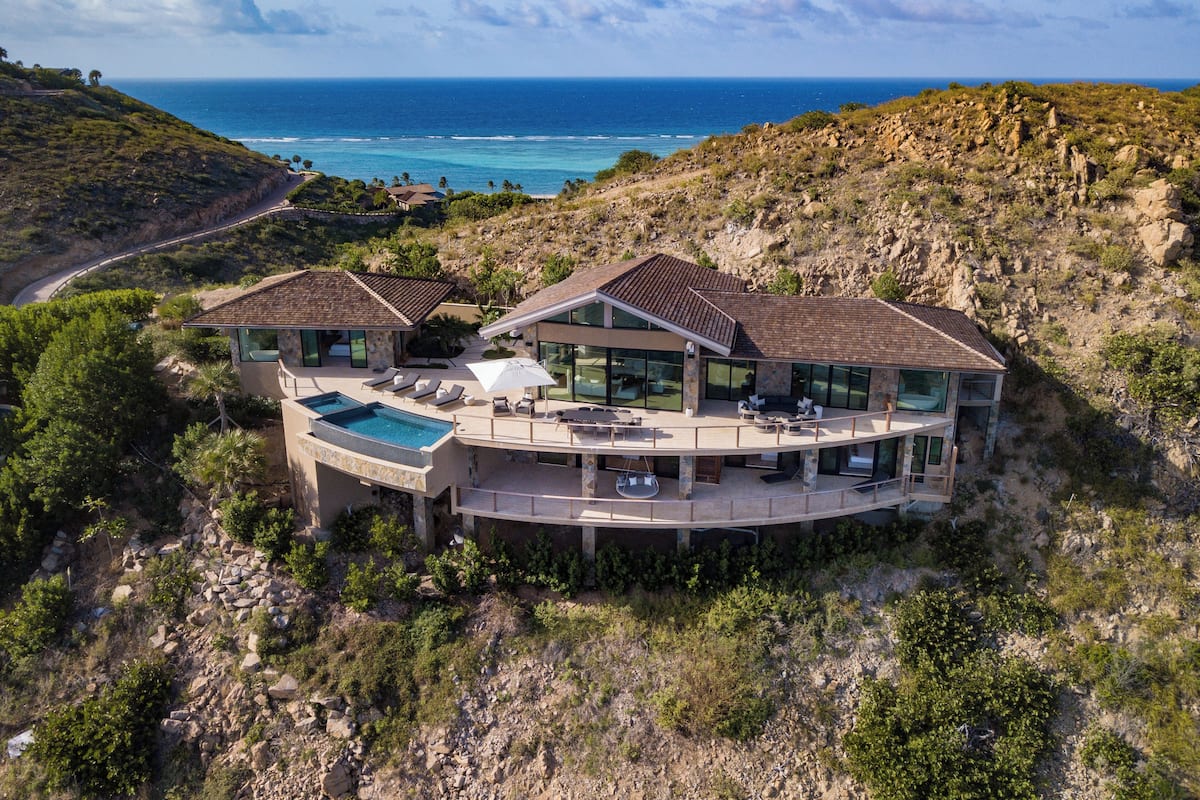 A modern villa with a large swimming pool, outdoor seating, and a view of the ocean.