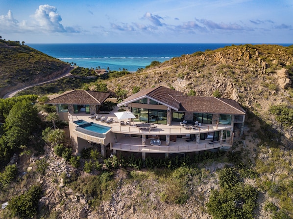 A modern villa with a large swimming pool, outdoor seating, and a view of the ocean.