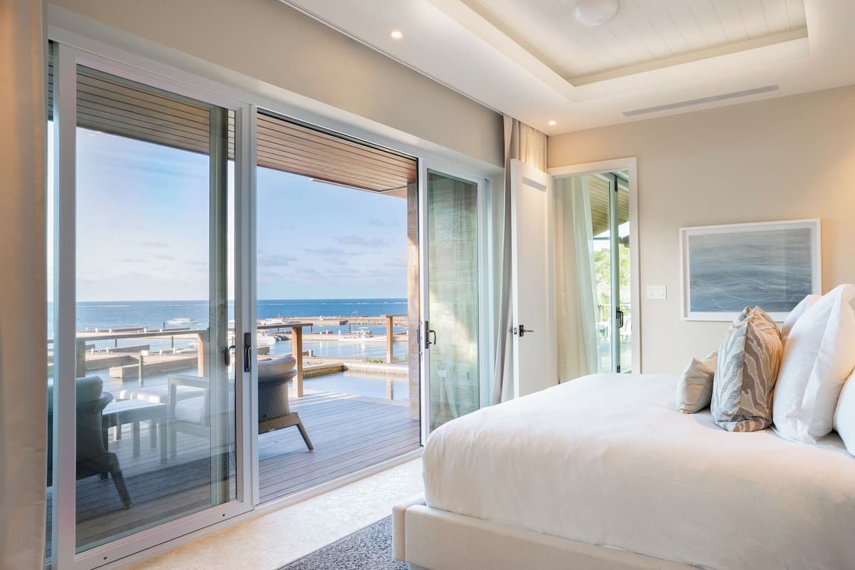 A bedroom with a large bed, a view of the ocean, and a balcony with outdoor furniture.
