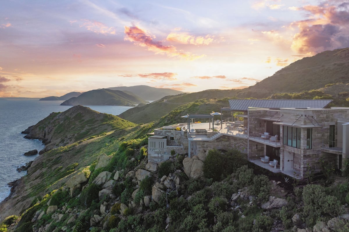 A coastal property with a stone house, outdoor seating, and a view of the sea and hills.