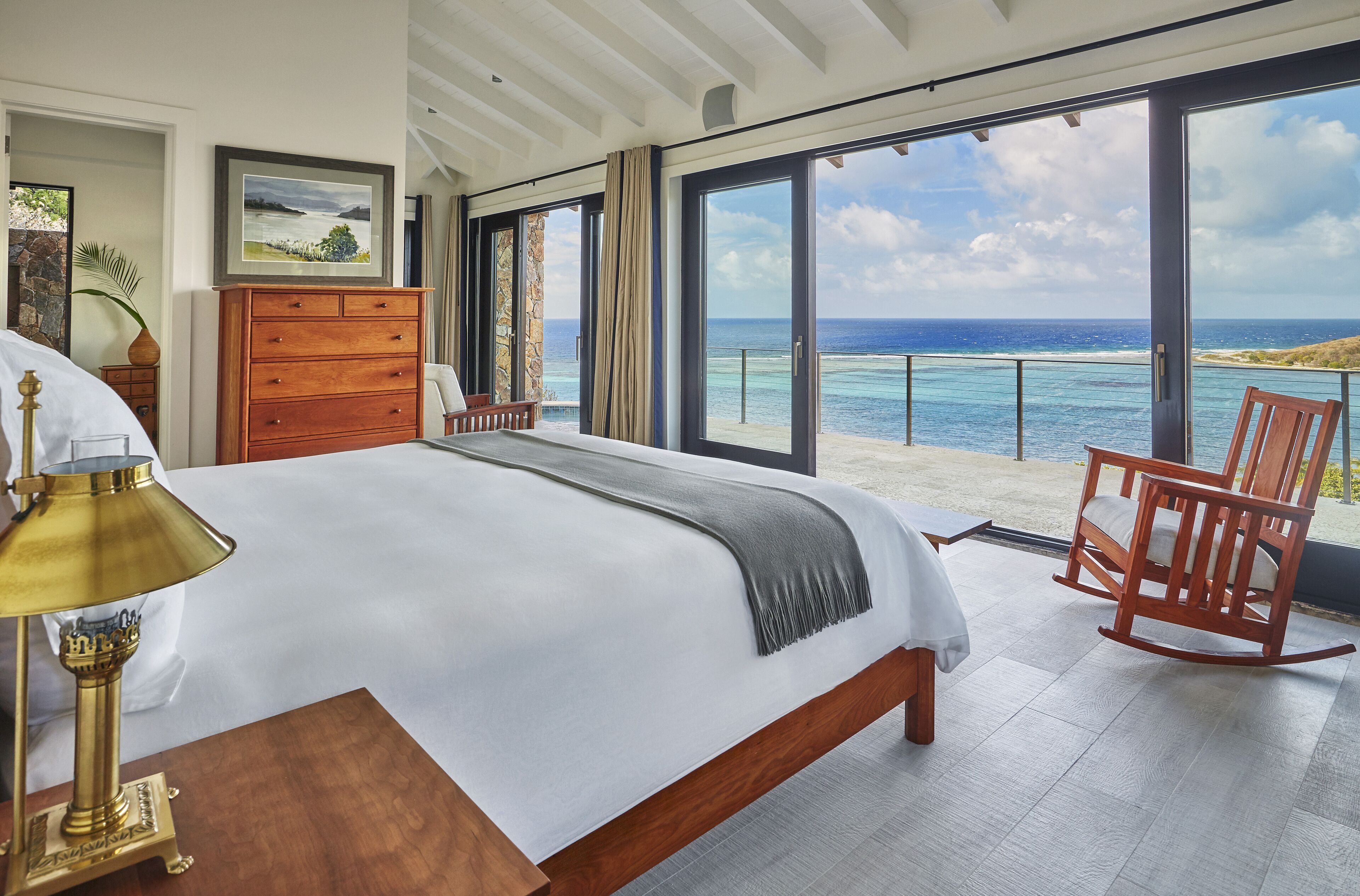 Un dormitorio con una cama grande, un aparador de madera, una mecedora y vista al océano.