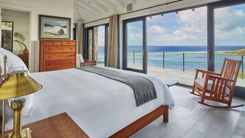 Un dormitorio con una cama grande, un aparador de madera, una mecedora y vista al océano.