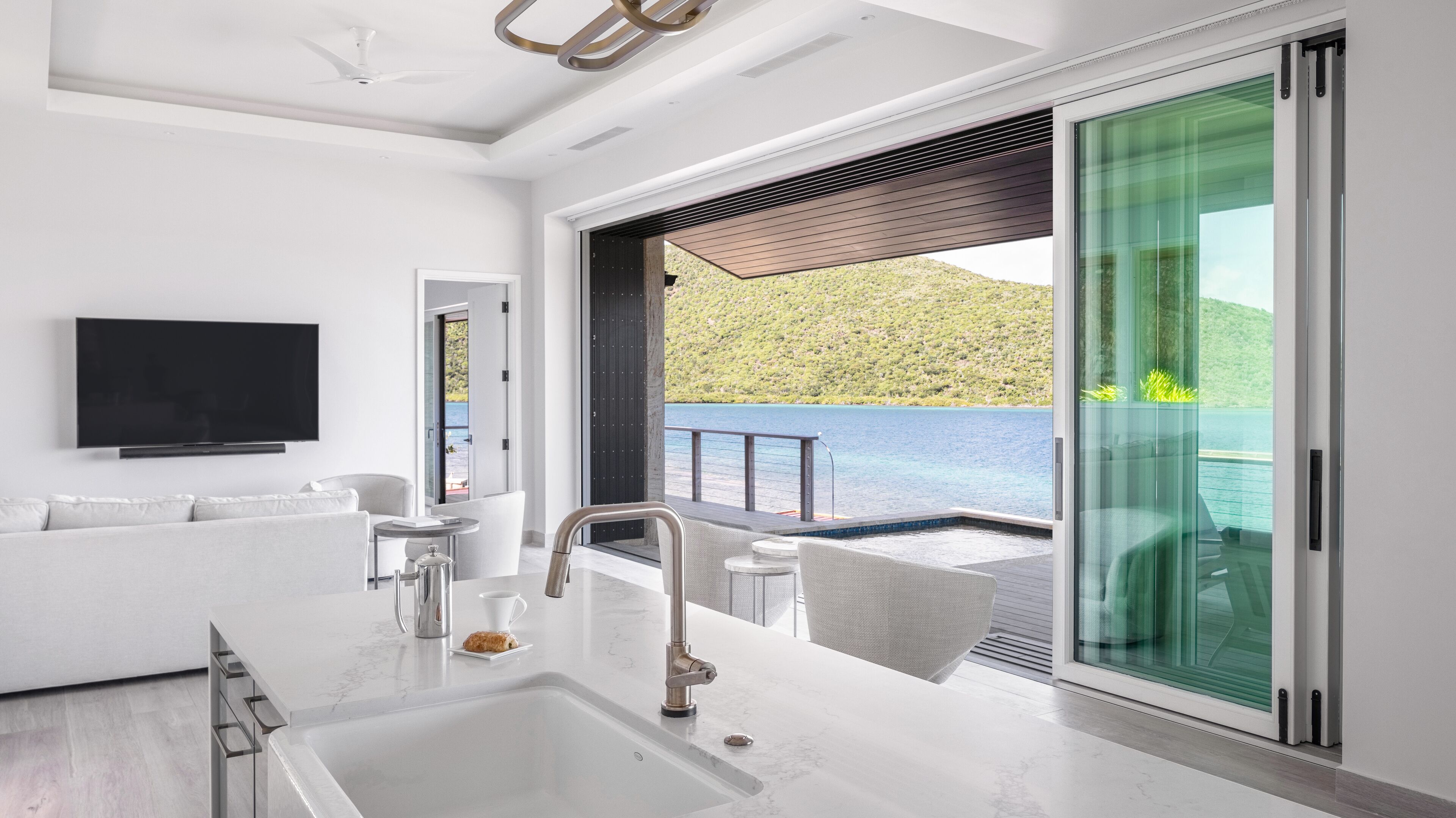 Una sala de estar moderna con un televisor grande, un sofá, una mesa de centro y una zona de cocina con un lavaplatos.