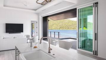 Una sala de estar moderna con un televisor grande, un sofá, una mesa de centro y una zona de cocina con un lavaplatos.