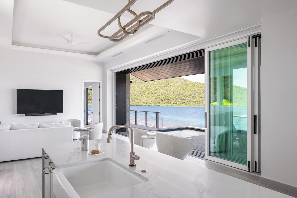 A modern kitchen with a large island, a flat-screen TV, and a view of a mountainous landscape through a sliding glass door.