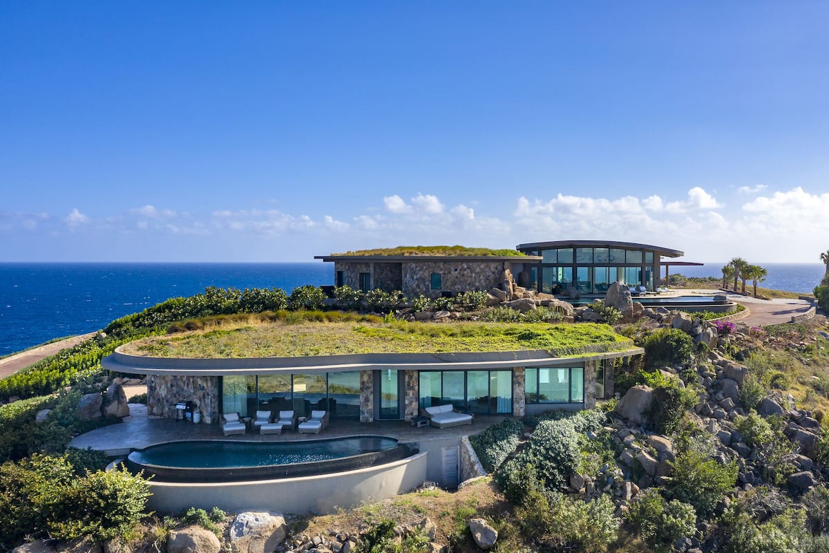 A modern coastal house with a large glass pool, outdoor seating, and a view of the ocean.
