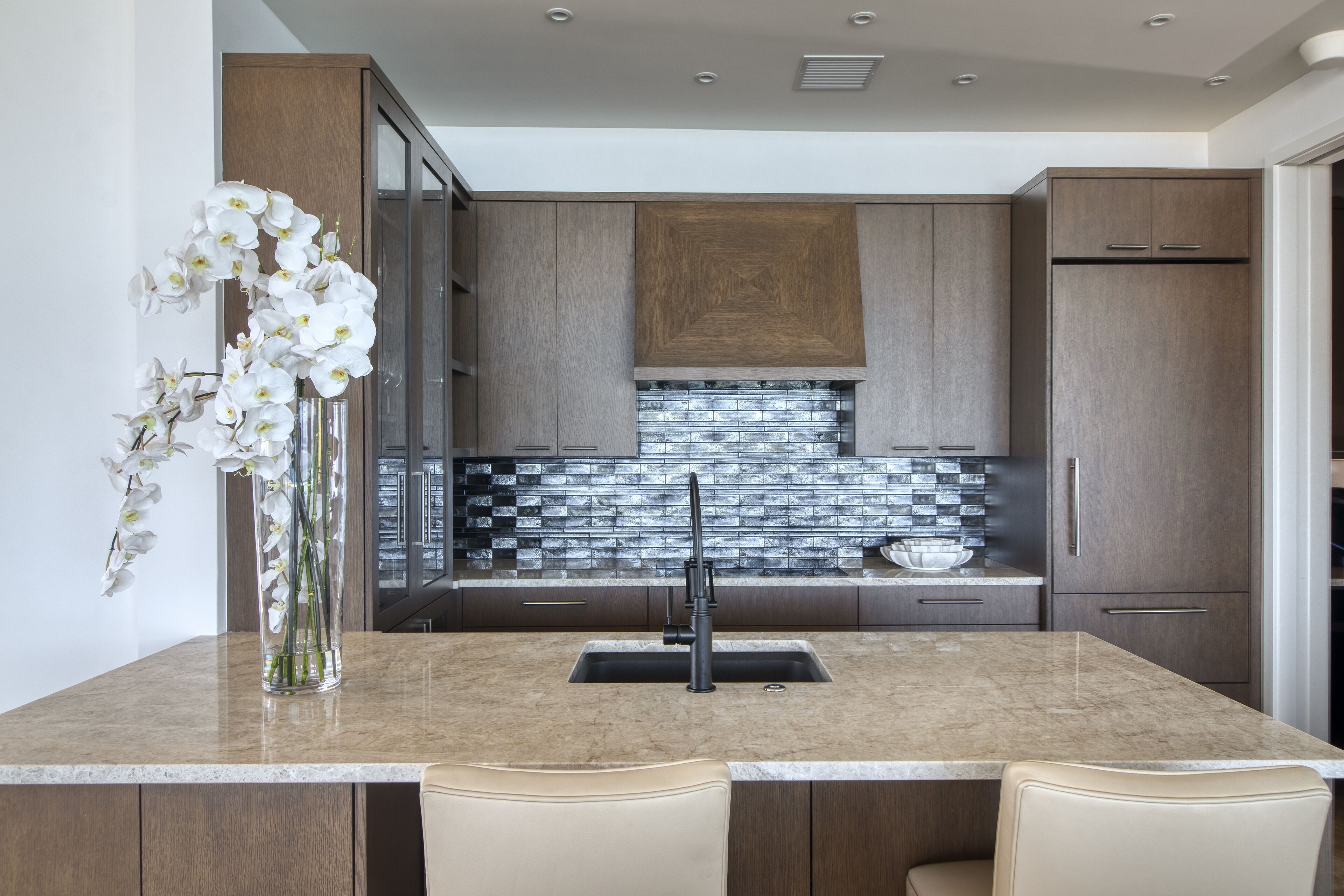 A modern kitchen with a marble countertop, a sink, and a vase of white orchids.