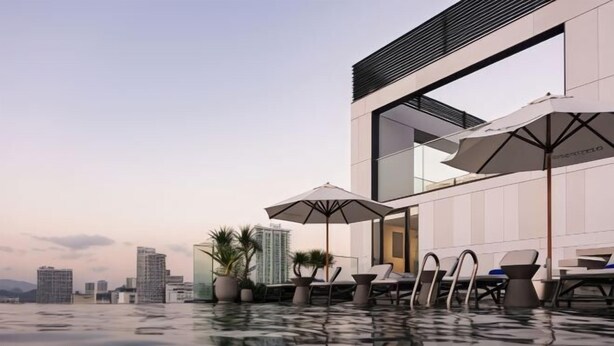 A rooftop infinity pool with lounge chairs and umbrellas, surrounded by modern buildings. - December Hotel (Nha Trang)